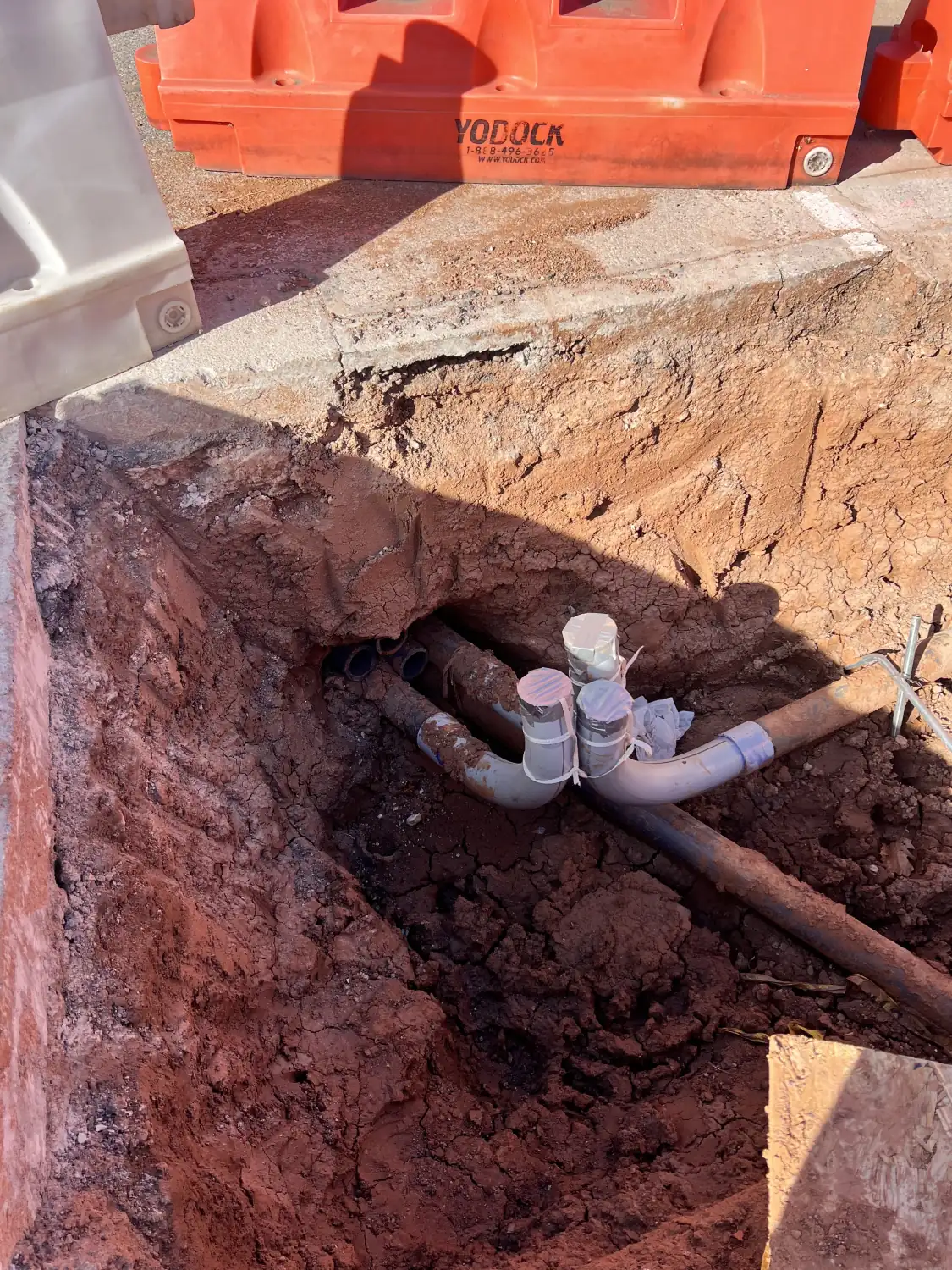 Open bore pit in red Oklahoma dirt with white PVC conduit stub-ups and an orange safety barrier