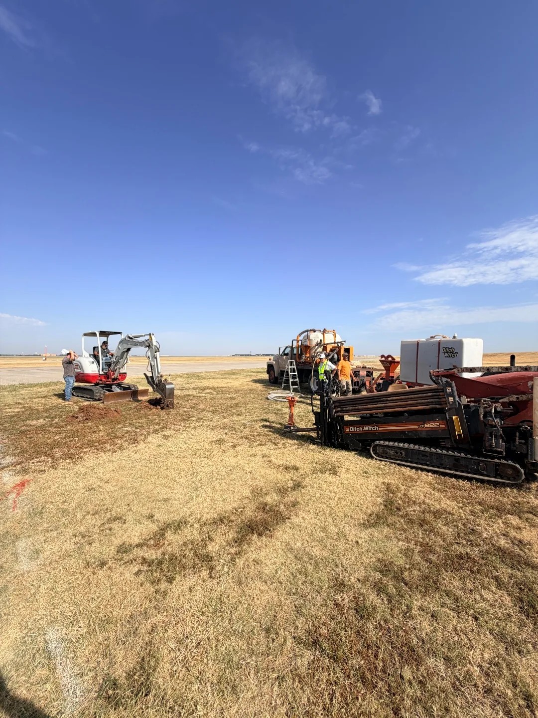 Mini excavator opening a bore pit beside a Ditch Witch directional drill rig on the airfield at Will Rogers World Airport