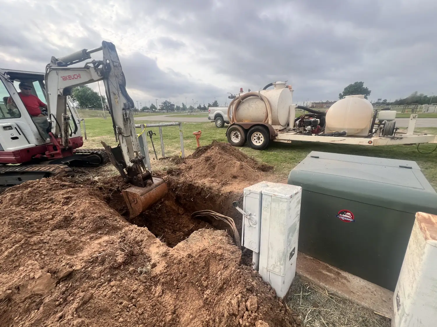 Mini excavator digging beside a pad-mounted transformer on a Trinity Boring Solutions jobsite in Oklahoma