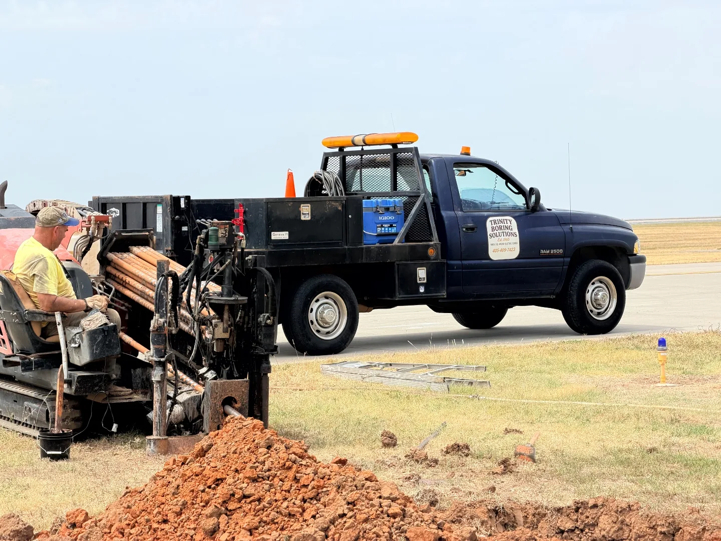 Ditch Witch JT922 directional drill rig boring beneath an airport taxiway next to a Trinity Boring Solutions truck at Will Rogers World Airport